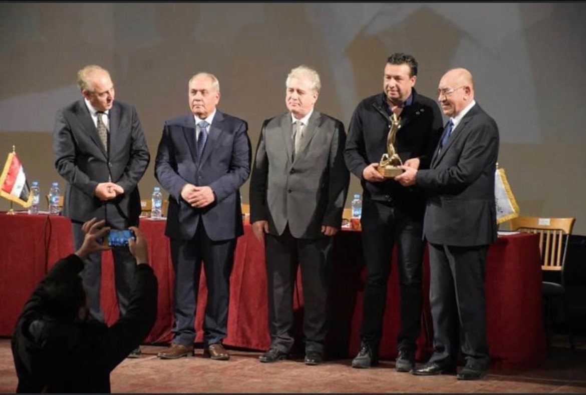 علاء حجو يتسلم جائزة من غرفة الصناعة السورية على المسرح.